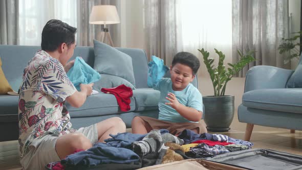 Excited Asian Young Dad And Son Packing Clothes In Suitcase At Home, Preparing For Their Vacation alt