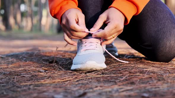 Female runner kneeling and tying shoelace preparing for a run on a forest trail in the morning. alt