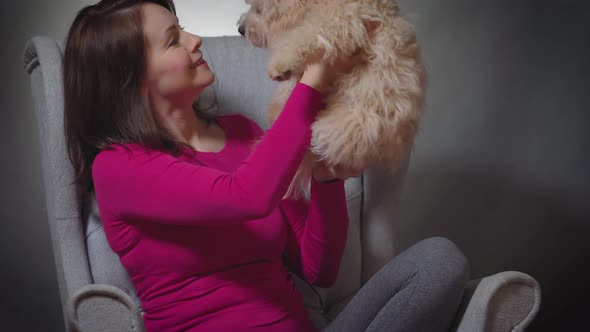 Beautiful Woman Is Playing with a Small Puppy on Chair
