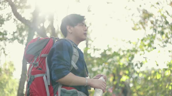 Asian man tourists drinking water while resting in the forest on a sunny beautiful summer day. alt