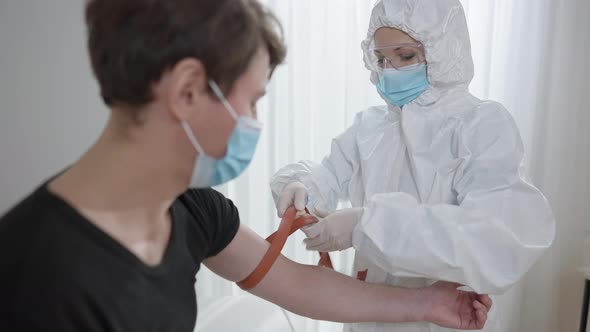 Focused Woman in Protective Suit and Coronavirus Face Mask Tightening Harness on Hand of Man alt