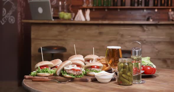 A Wooden Table with Burgers on Wooden Boards in Front of a Bar alt