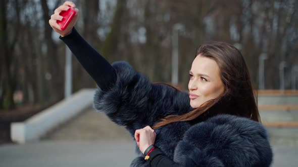 Girl with smartphone in hand. Lifestyle portrait of young positive woman making selfie in park alt