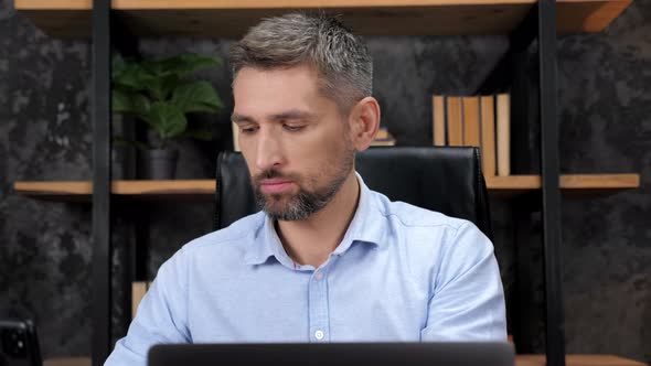 Businessman Inserts Wireless Earphones Into Ears Works for Laptop in Office alt