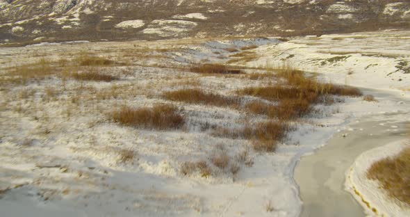 Aerial helicopter shot, lift over small river and barren trees, to reveal river valley, mountains in alt