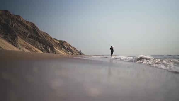 Man Walking Along Beach As Tide Comes In alt