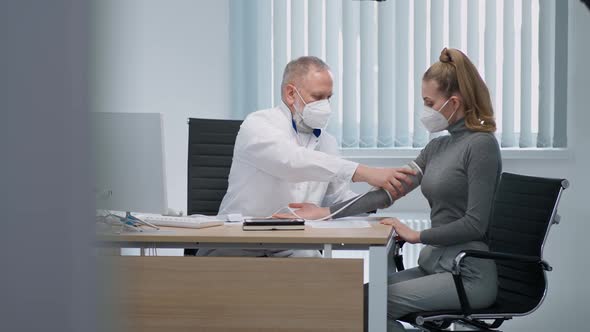 Modern Private Clinic Grayhaired Adult Male Doctor Measures the Blood Pressure of a Young Female alt