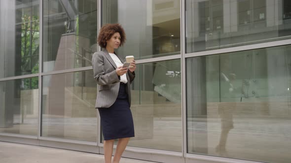 Afro American businesswoman in city using smart phone with takeaway coffee