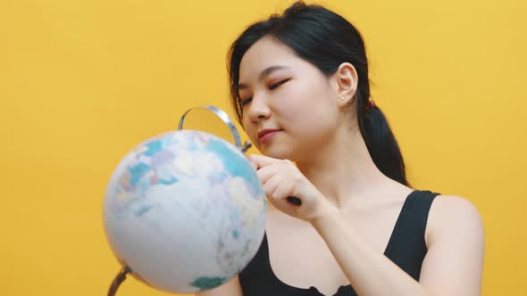 Young Asian Woman Examining the Globe with a Magnifying Glass alt