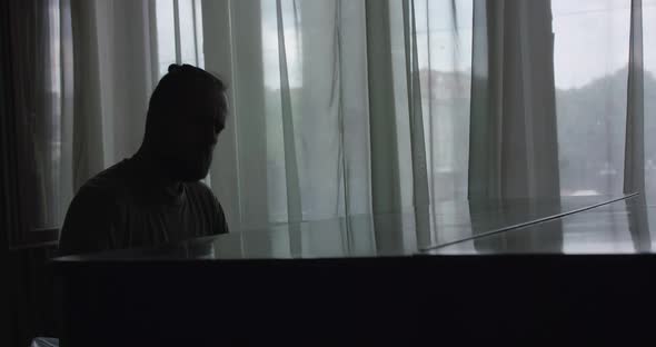Silhouette of Man Playing the Piano Gracefully and Having Pleasure in a Lobby alt