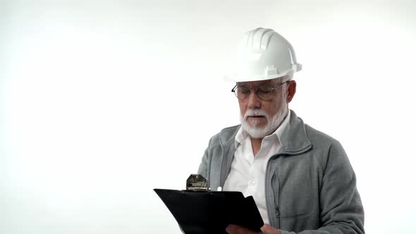 A Bearded Elderly Pensioner Man in a Construction Helmet Writes Annotations with a Pen on a Writing