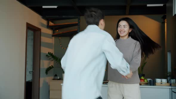 Asian Woman and Biracial Race Man Dancing and Having Fun Together in Modern Kitchen alt