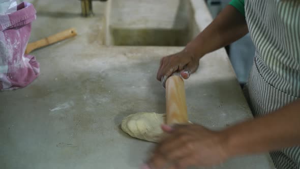 Mature Latin woman kneading flour dough with rolling pin in old vintage kitchen alt