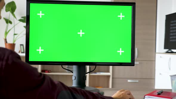 Side View of Man Sitting in Front of Computer with Big Green Screen Mock-up Chroma Typing on the alt