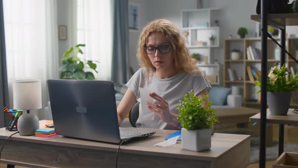 Young Woman at the Desk in the Living Room Counts the Costs in Checks alt