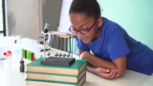African American Mixed Kid Pulling a Newton's Cradles Ball Swing in Science Classroom alt