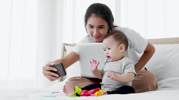 Mother works with laptop and plays with her baby infant. Busy single mother concept