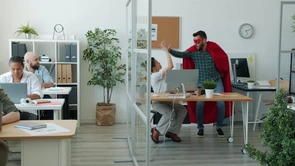 Funny Young Man in Super Hero Costume Running in Office Doing Highfive with Colleagues alt