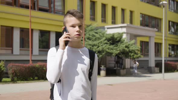 A Caucasian Teenage Boy Talks on a Smartphone  a School in the Background