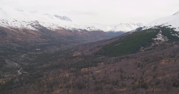 Aerial helicopter shot of Alaskan highway alongside river, over houses in the trees, drone footage alt