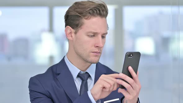 Portrait of Cheerful Young Businessman Using Smartphone in Office alt