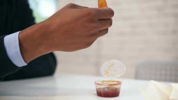 Young African American Dips Chicken Nugget in Sauce and Eats It Looking in the Camera During Lunch alt