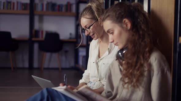 Female College Students Learning Together and Reading Books in University Library on the Floor alt