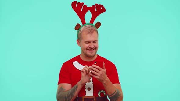 Man in Christmas Tshirt Using Mobile Phone Typing New Post on Web Shopping Online Show Thumbs Up alt