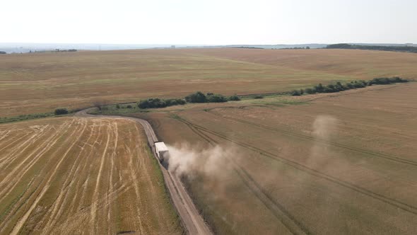 Aerial View of Lorry Cargo Truck Driving on Dirt Road Between Agricultural Wheat Fields alt
