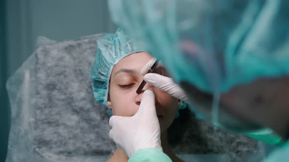 Surgeon Examines Girl's Face Before Rhinoplasty Surgery Drawing on Her Nose