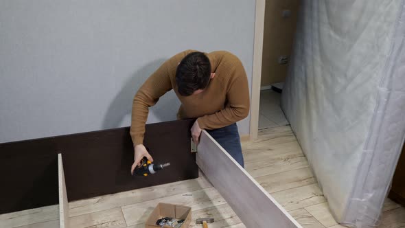 Young Man in Brown Sweater Assembles the Bed with a Screwdriver alt