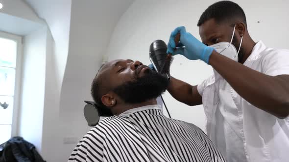 Barber blow-drying and brushing beard of customer alt