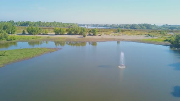 Fountain in Lake at Meadow Against Blue Sky Upper View alt