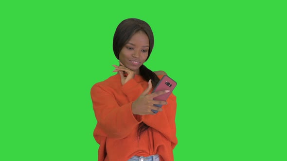 Smiling African American Woman in Bright Jumper Taking Selfie and Checking Her Phone on a Green alt