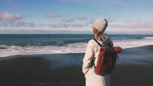 Tourist Woman with Leather Bagpack Standing Near the Coastal Landscape in Iceland alt