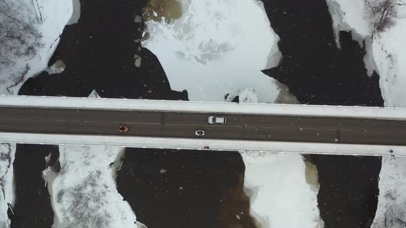 Aerial view of Cars driving on a bridge over frozen river in winter snowstorm