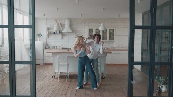 Happy Funky Young Romantic Couple Dancing Jumping in Kitchen alt