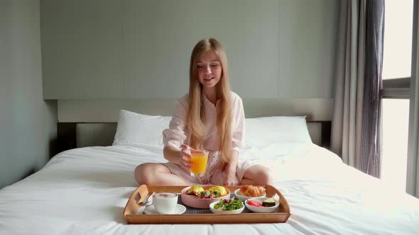 Young Smiling Beautiful Woman Eating Breakfast in Bed in Cozy Hotel Room alt