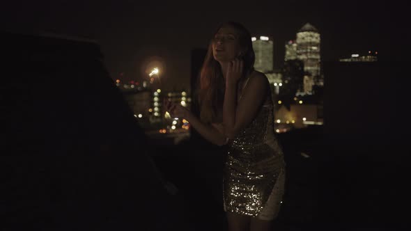 Young adult woman dancing on rooftop with sparkler