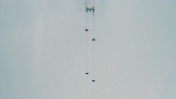 Aerial view of people going up a snow capped mountain with a chairlift, going down skiing and doing alt