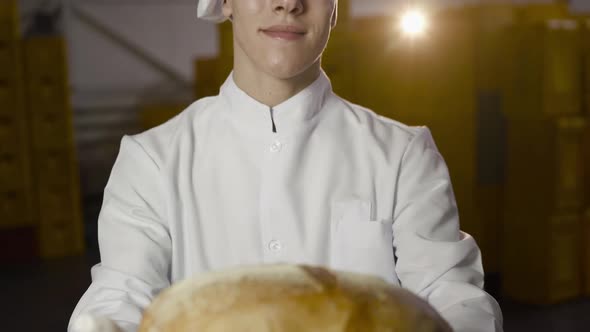 Baker in Uniform Presents Close at Camera Freshly Baked Loaf of Bread in Bakery alt
