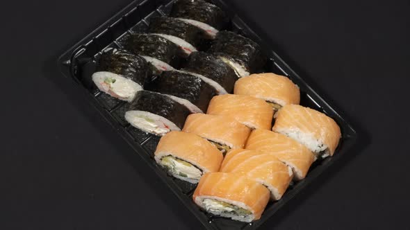 Sushi Rolls Rotates in a Plastic Container on a Black Background. Meal Delivery alt