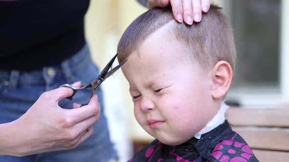 Portrait of a Little Baby Boy with Closed Eyes and Scaring Emotions While Hairdresser Cuts His alt