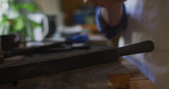 Caucasian female jeweller in workshop wearing apron, using gas burner, melting metal alt
