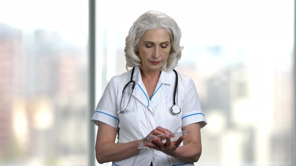 Mature Doctor Using Glass Tablet on Blurred Background. alt