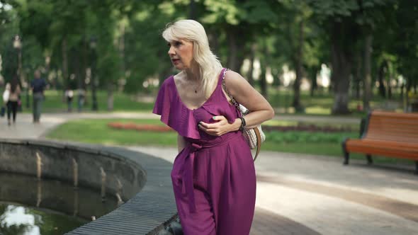 Adult Woman Walking in Park Having Heart Ache Sitting Down at Fountain Taking Pills alt
