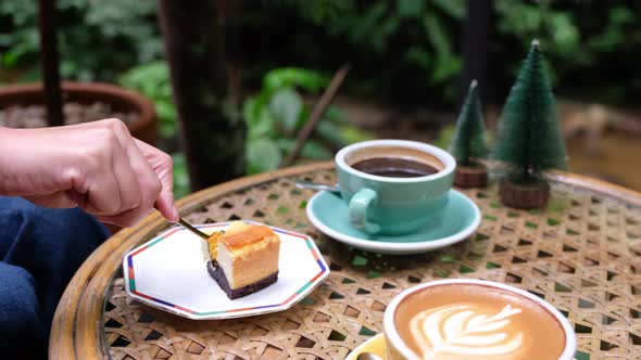 A woman eating a piece of cheesecake and coffee in outdoors cafe