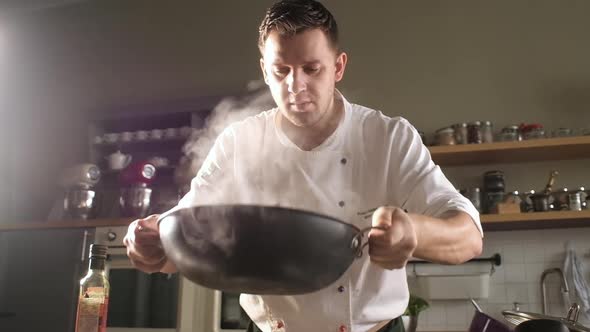 chef in modern kitchen mixes ingredients in wok. man throws pasta in the pan. alt