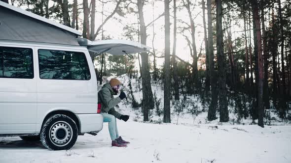 Man Drinks Sitting in the Back of a Van with Pop Up Roof in the Woods in Winter