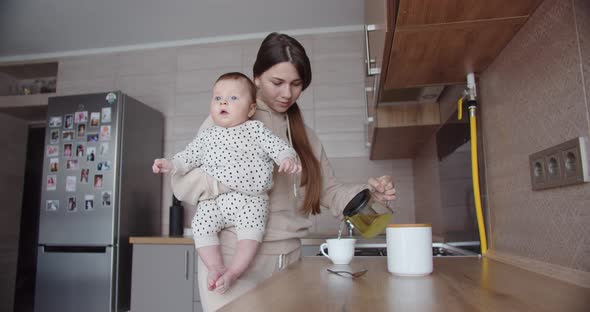 Mom With A Little Baby In Her Arms Prepares Breakfast